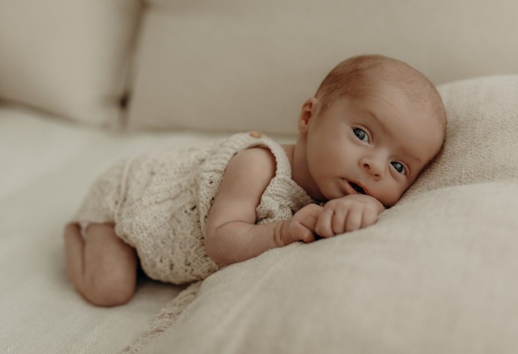 Neugeborenes Baby liegt auf dem Sofa und blickt in die Kamera beim Newborn Shooting
