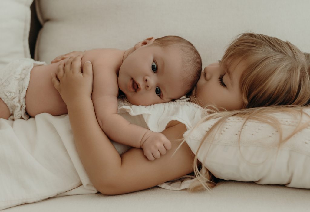 Inniges Geschwisterbild von kleinem Baby und großer Schwester beim Babyfotoshooting