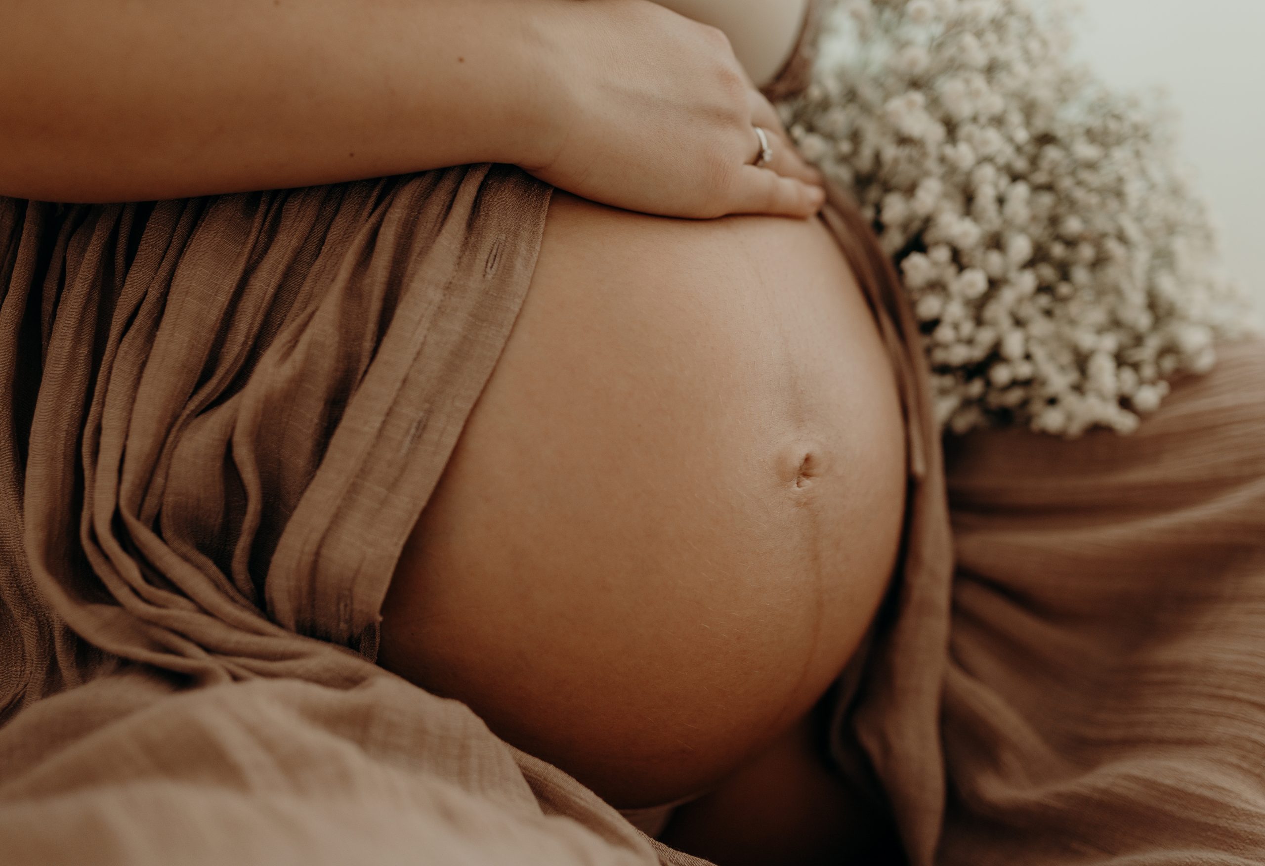 Frau legt Hand auf Babybauch im Hintergrund sind Blumen neben dem Babybauch