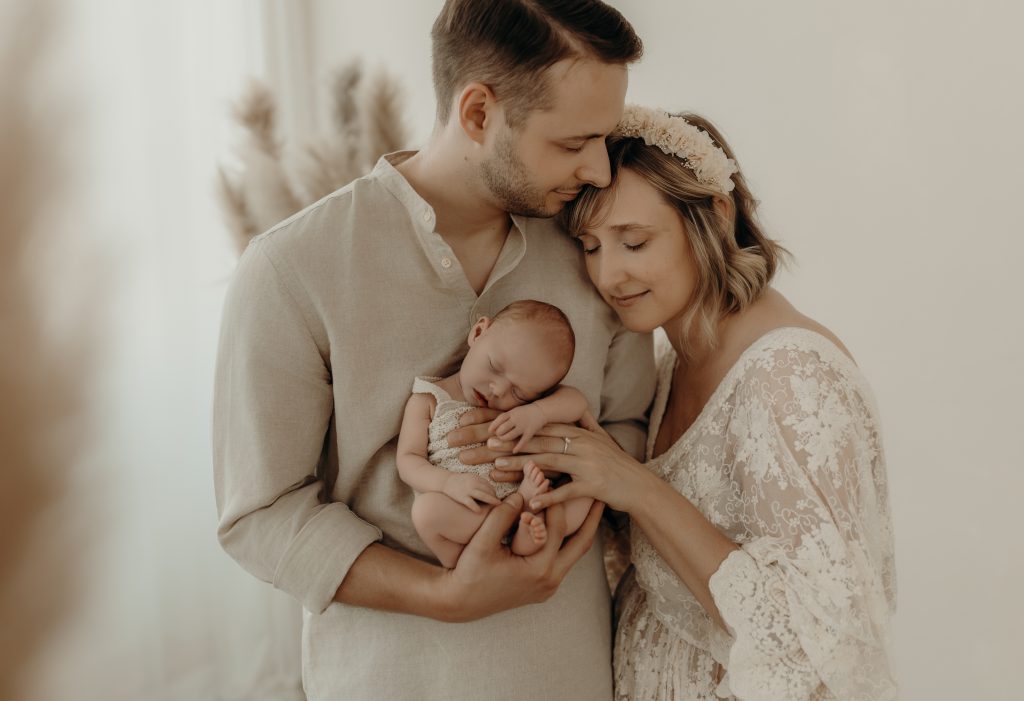 Familie mit Mama Papa und Baby kuscheln sich zusammen mit geschlossenen Augen