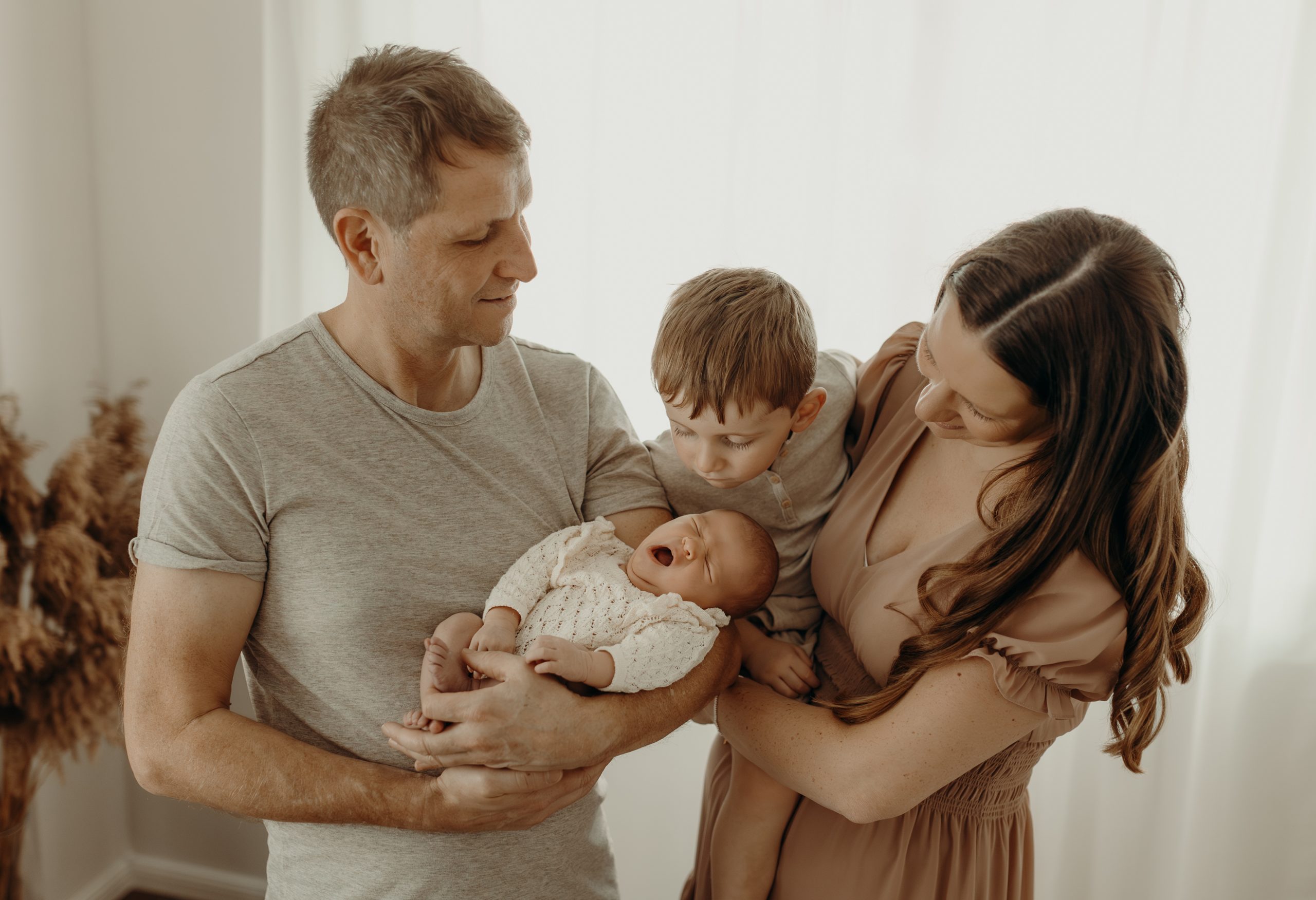 Mama Papa und großer Bruder schauen auf die kleine Babyschwester im Arm