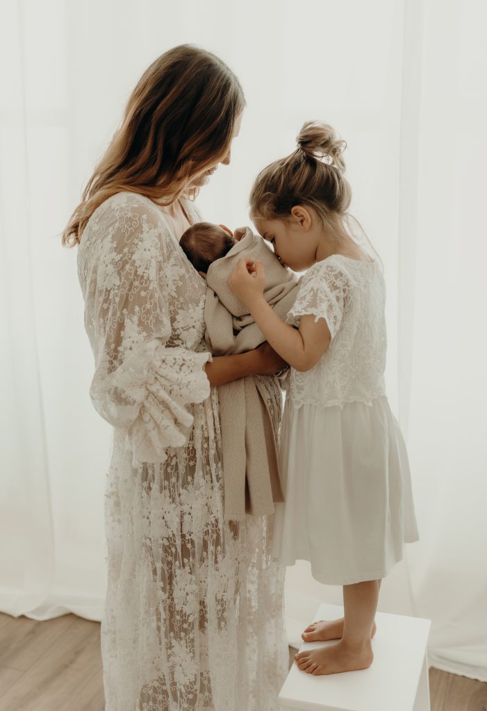 Mama hat Baby auf dem Arm was eine Kuss von der großen Schwester bekommt