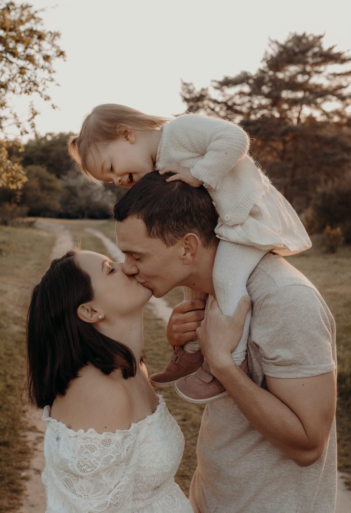 Mama und Papa küssen sich beim Outdoor Fotoshooting mit kleiner Tochter