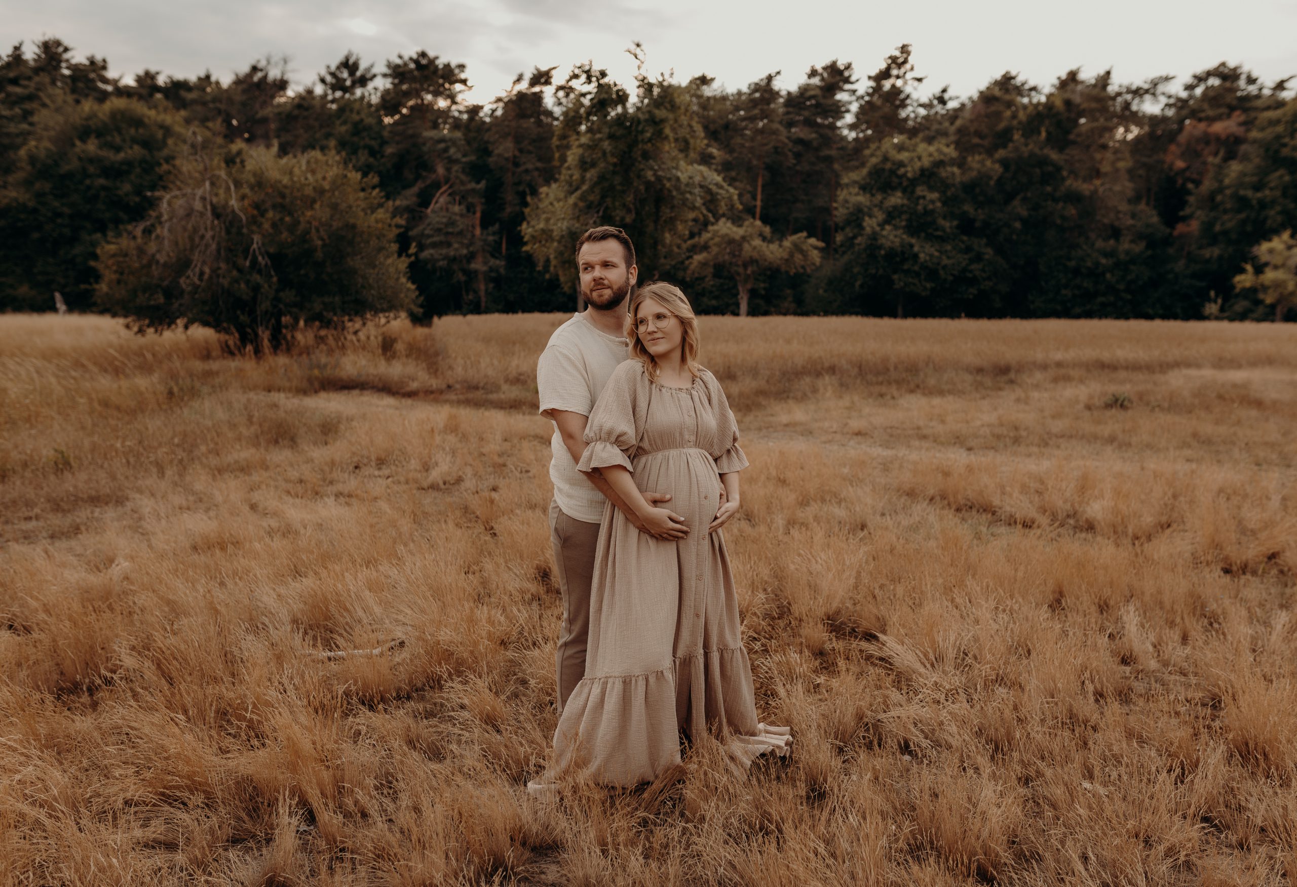 Paar steht beim Babybauch Shooting in Frankfurt in der Natur und blickt zur Seite