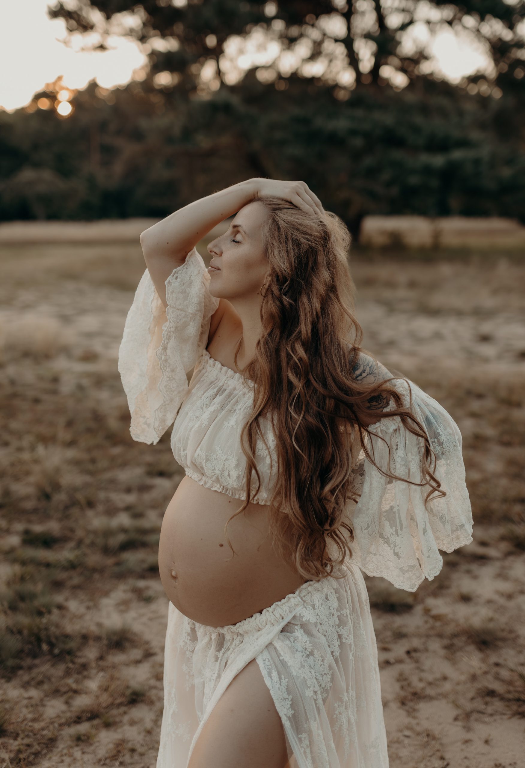 Schwangere Frau steht beim Babybauch Shooting in der Natur bei Frankfurt und streicht sich die Haare nach hinten